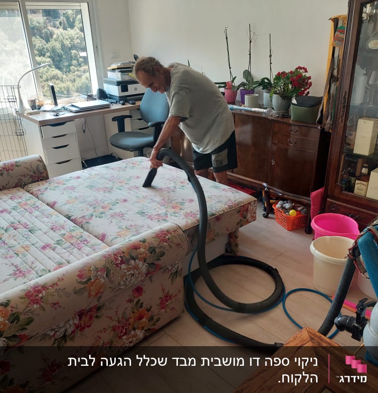 אדם מנקה ספה עם שואב אבק בחדר.
